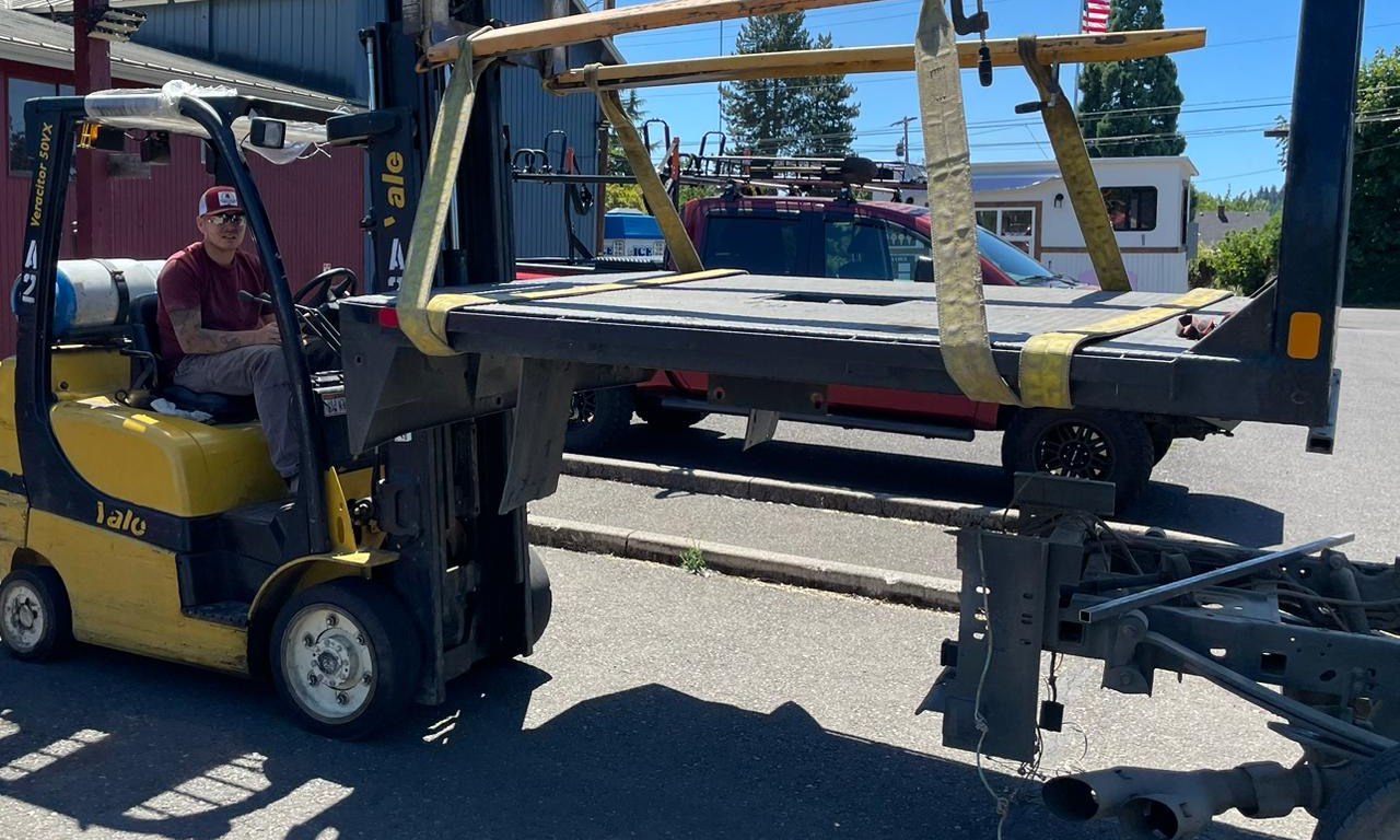 Crystal Creek crew using a forklift to position a custom black metal truck platform over a chassis