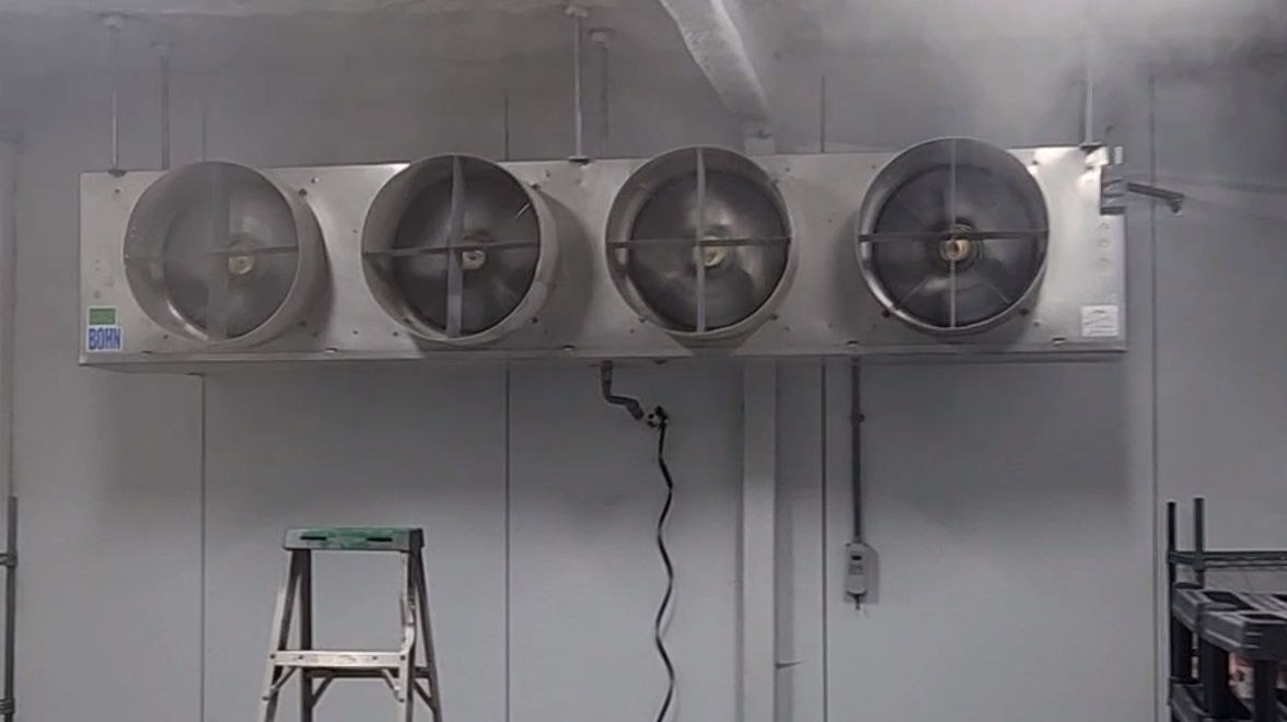 Four-fan commercial evaporator unit in a misted cold room with product shelving